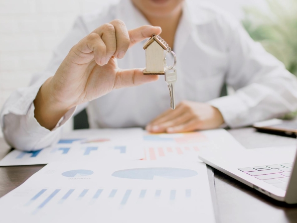 Real estate professional presenting a house model with keys, symbolizing property investment and ownership.